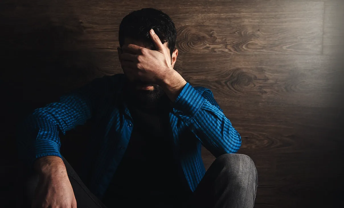 Pessoa sentada de cabeça baixa em ambiente com pouca luz, representando o sofrimento da depressão